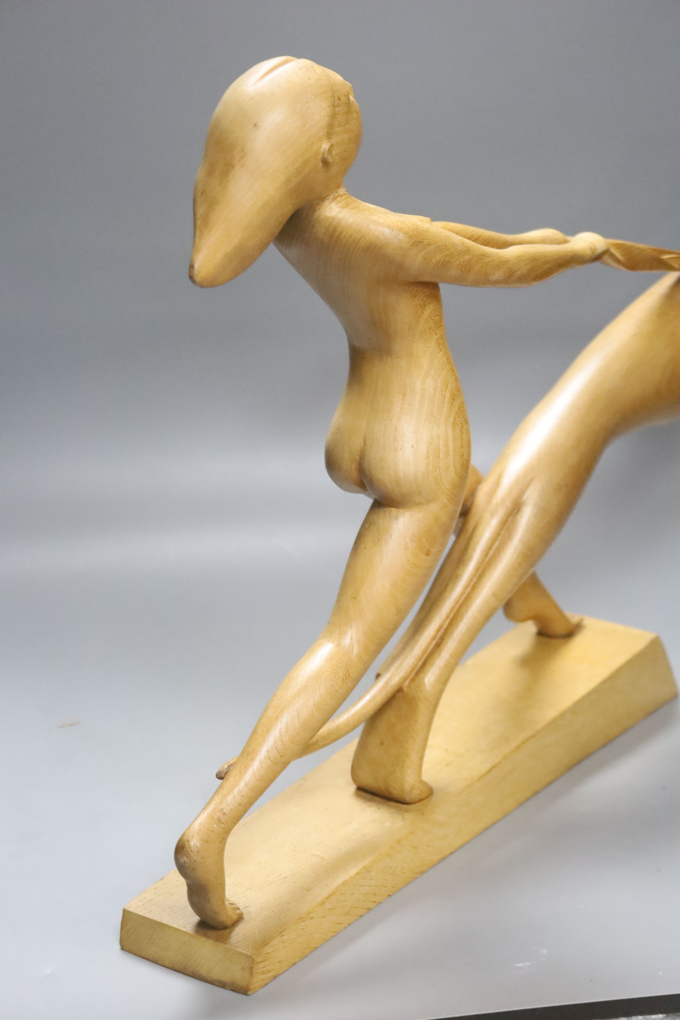 An Art Deco style light elm carving of a woman and dog on lead-weighted plinth, height 40cm